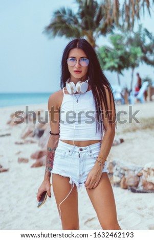 Beauty woman listening music on headphones, outdoor hipster portrait, purple hair, fashion model, color, sunglasses, smartphone, tattoo, smartphone, orange wall, happy face, smile, hipster style
