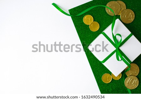 The composition of the St. Patrick's day. White gift box with green bow and gold coins on a green shiny and white background with copy space