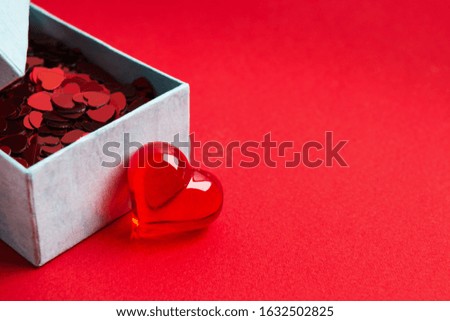Holiday confetti of heart shape in box for wedding or Valentine's day, Gift of love. Love concept in present box over red background with glass heart. Selective focus