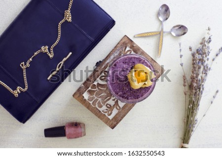Getting ready in the morning concept picture with clutch purse and nail varnish, blueberry smoothie for two in same glass, saving dishes, jewellery crest underneath. Flatlay photo.