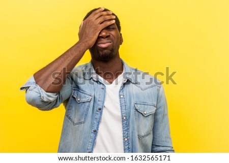Facepalm, I forgot. Portrait of regretful man in denim casual shirt holding hand on face, feeling sorrow and desperation about failure, his fault. indoor studio shot isolated on yellow background Royalty-Free Stock Photo #1632565171