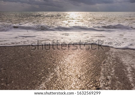 Sunny sunset or sunrise seashore, cloudy dramatic heaven and foamy splashing sea waves at sandy seashore. Beautiful natural photo background.