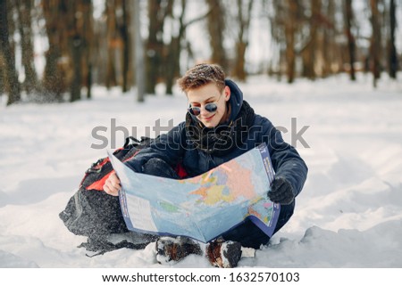 young and handsome guy sitting in the winter snow-covered forest with map
