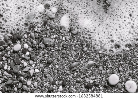 Closeup top view black and white photography of beautiful sandy beach with splashing foamy sea water. Abstract natural background.