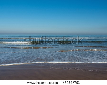 Gentle waves rolling into the beach on a sunny day, with a perfect blue sky and view of the  hazy horizon. 