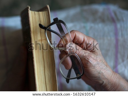 An elderly woman holds an old book in her hands. Old woman reading a book. Woman with reading glasses and a book.