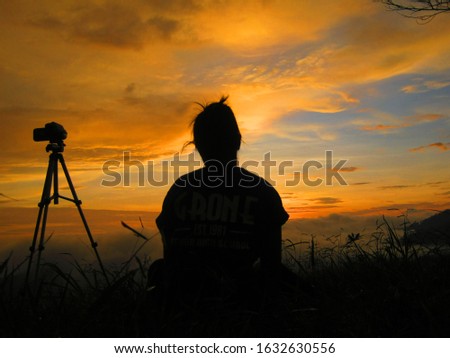 Photo of silhouette woman sitting beside tripods camera is looking to the sun rises on the mount top. perfect picture for travel addict.