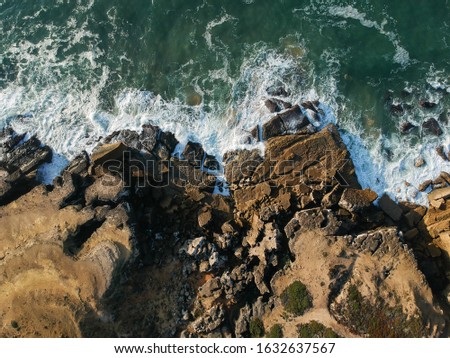 Aerial top view of sea waves hitting rocks