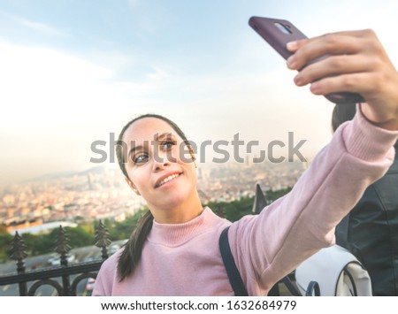 Young girl in pink is holding smartphone and making a selfie with a background of the big city -Istanbul in Turkey. Social media face. Touristy place with young people.