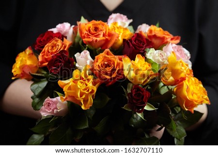 Bouquet of different color roses in female hand on a black background. Red, orange and pink flowers. Romantic Valentine's Day Gift