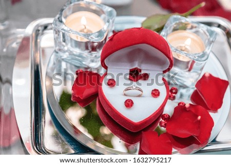 Wedding ring in rose petals against the background of candles.