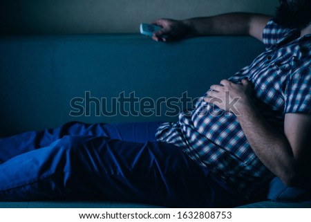 sedentary lifestyle, depression, lack of physical activity, sedentariness. overweight man with tv remote on the coach Royalty-Free Stock Photo #1632808753
