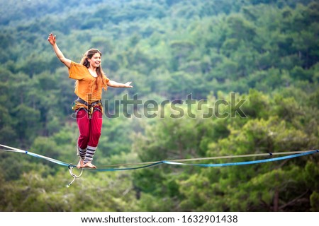 Highliner on a rope. Highline on a background of mountains. Extreme sport on the nature. Balancing on the sling. Equilibrium at altitude. A woman catches balance on the line.  Royalty-Free Stock Photo #1632901438