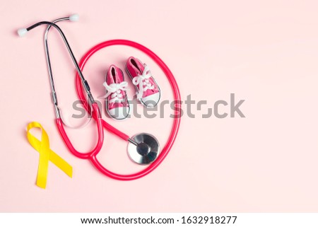 Childhood Cancer Awareness Golden Ribbon with blue baby sneakers and stethoscope on pink background with copy space. Childhood Cancer Day February, 15.