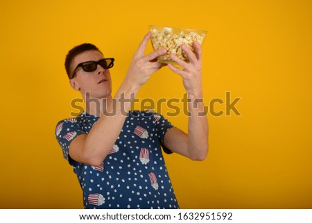 man in 3D glasses looks at a plate with popcorn on a yellow isolated background