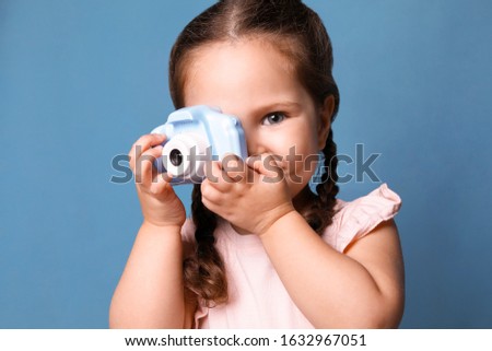 Little photographer taking picture with toy camera on blue background