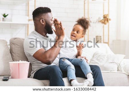 Let's watch TV together. Black father and little daughter giving high five, home interior, free space