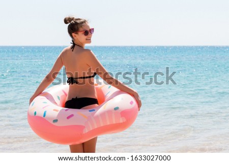 Fit woman with donut inflatable ring is walking into the sea to swim.