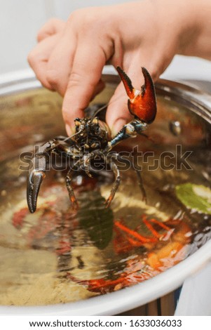 hand puts fresh crawfish in a pan with bowling water and spices