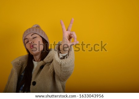 woman in hat with closed eyes signs fingers on yellow background