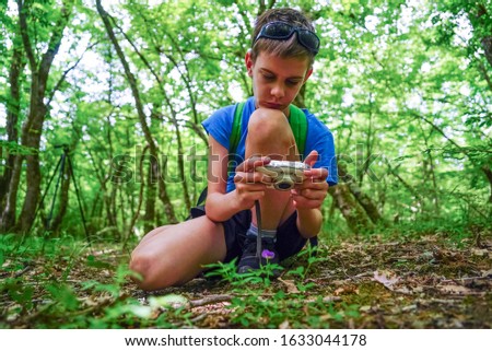 A boy with a camera shoots a flower in the forest.