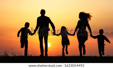 Silhouettes of happy family holding the hands in the meadow during sunset. Happy family enjoying life together. Happy young family spending time together outside in green nature.