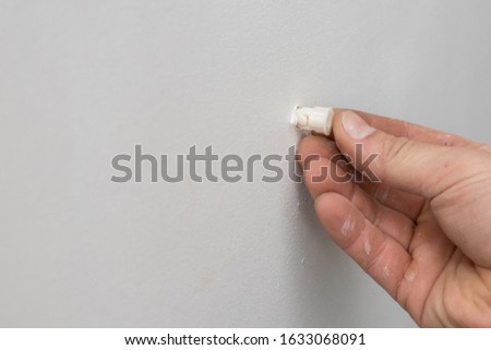 male hand pokes a plastic dowel into a white drywall wall, side view