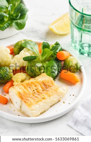 Grilled cod fillet with steamed vegetables: baby carrots, Brussels sprouts, broccoli, cauliflower and corn salad on a white plate. Healthy food. Close-up. Selective focus.