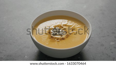 closeup pumpkin cream soup in white bowl on terrazzo countertop