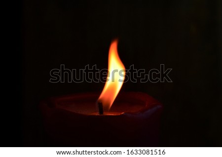 Burning single red candle with dancing flame on the dark background