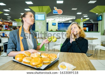 woman with a girl in a cafe. mom puts aside fast food and gives the fat girl apples. the problem of proper, healthy nutrition in children. teen refuses fruit and chooses burgers