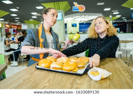 woman with a girl in a cafe. mom cleans fast food and gives the fat girl apples. the problem of proper, healthy nutrition in children. teen refuses fruit and chooses burgers