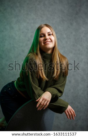Girl in a green sweater and jeans on a gray chair and smiling