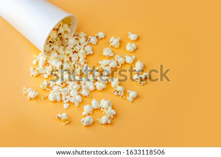 Fresh popcorn spilled out of the white box on a orange background. Cinema snack concept. The food for watching a movie and entertainment. Copy space for text, close up. Popcorn box mocap