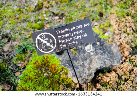 Improvised sign warning people to keep off a delicate garden rockery whereby alpine plants are growing.