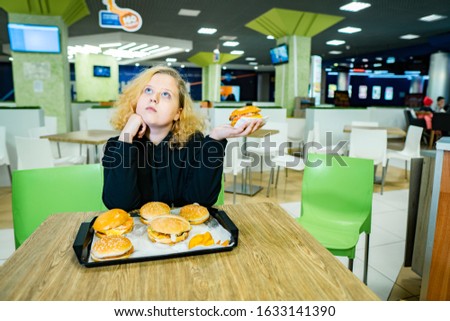 child in cafe fast food. teen girl ordered a lot of hamburgers