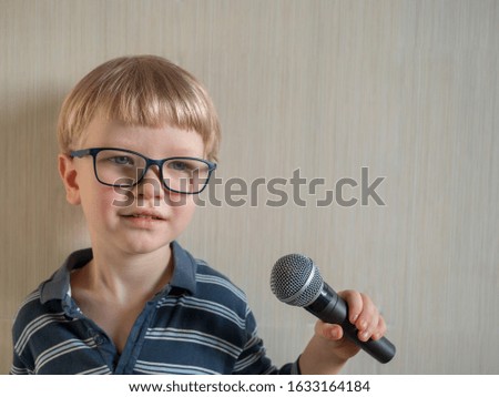 Funny blond boy in big eyeglasses holds in his hands microphone for karaoke. White background, light from window