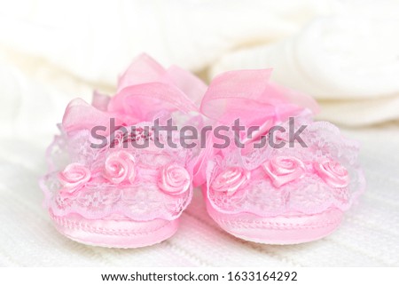 Pink baby booties from the front, on white crochet blanket. Shoes with lace, shiny ribbon and silk rose decoration.