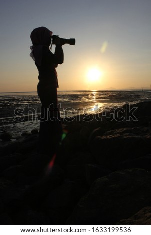 silhouette of young woman photographer, taking pictures of landscape at sunset