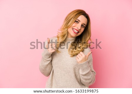 Young blonde cute woman wearing a sweater isolated raising both thumbs up, smiling and confident.
