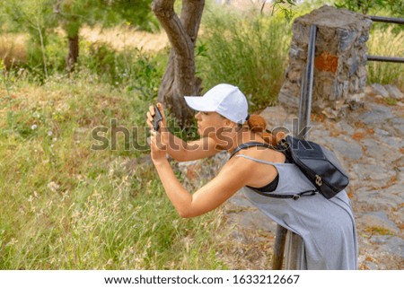 Tourist woman captures nature landscape on her smartphone, while hanging on the fence into the wild.
