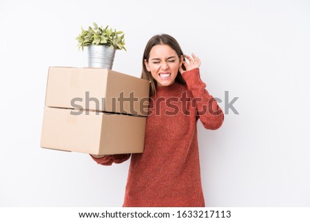 Young caucasic woman holding boxes isolated covering ears with hands.