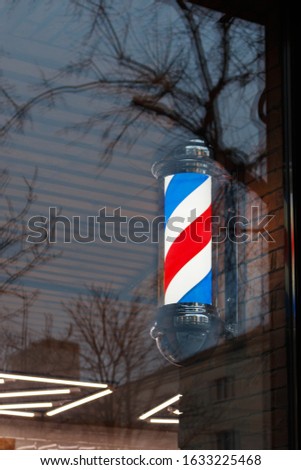 American barber pole sign with a helical stripe (red, white, and blue) in the barber shop window. masculinity and personal care concept

