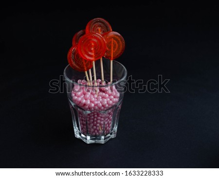 Several red candies on a stick on a black background in a glass