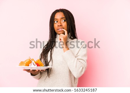 Young african american woman holding a waffle isolated relaxed thinking about something looking at a copy space.