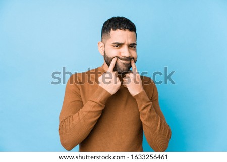 Young latin man against a blue  background isolated doubting between two options.