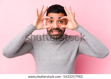 Young latin man against a pink background isolated keeping eyes opened to find a success opportunity.