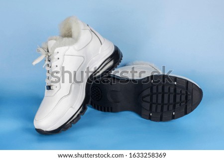 White women's low boots with white fur on blue background. Warm shoes for women and girls who love sports shoes for walking in winter and spring