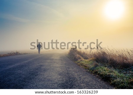 A person walk into the misty foggy road in a dramatic mystic sunrise scene with abstract colors Royalty-Free Stock Photo #163326239