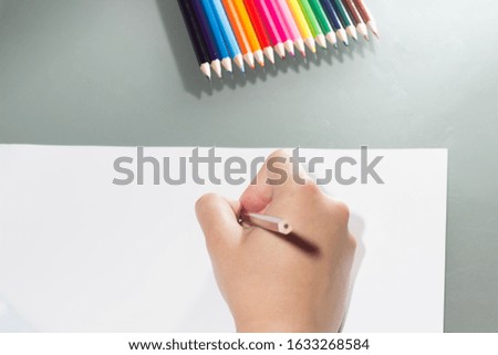 the girl draws on a white sheet of paper with colored pencils
